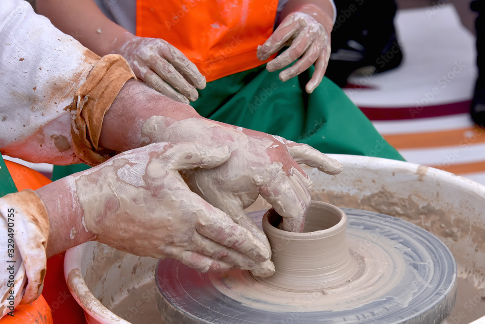 A human Potter works on a Potter's wheel, making a ceramic pot from clay in a pottery workshop.