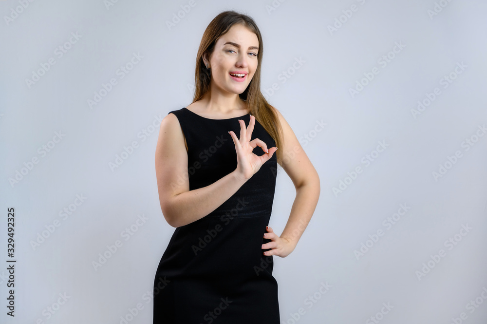 Portrait on a white background of a sympathetic Caucasian woman in a black dress shows her fingers ok with a smile Portrait on a white background of a sympathetic Caucasian woman in a black dress shows her fingers ok with a smile