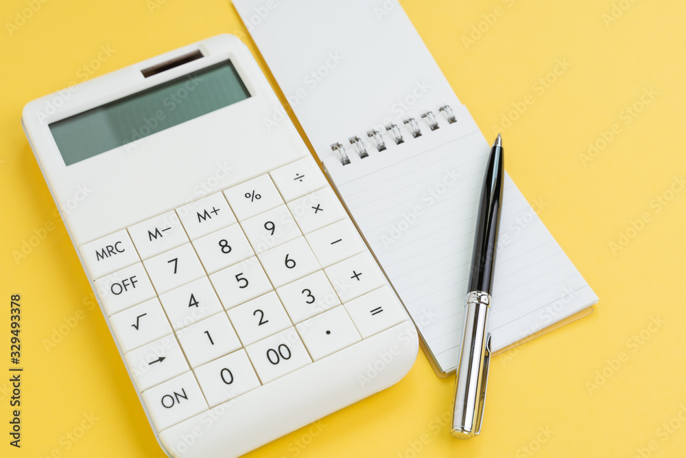 Pen with note paper and calculator on yellow background using as finance, budget planning or financial cost and expense calculation concept Pen with note paper and calculator on yellow background using as finance, budget planning or financial cost and expense calculation concept