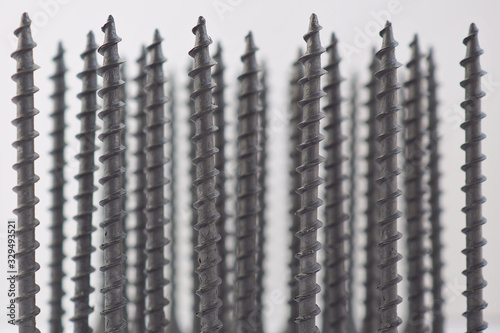 Background of self-tapping screws, black and long, standing upright. Reduced contrast. Hardware, ironware, ironmongery, fasteners, materials for construction and repair. Macro photo