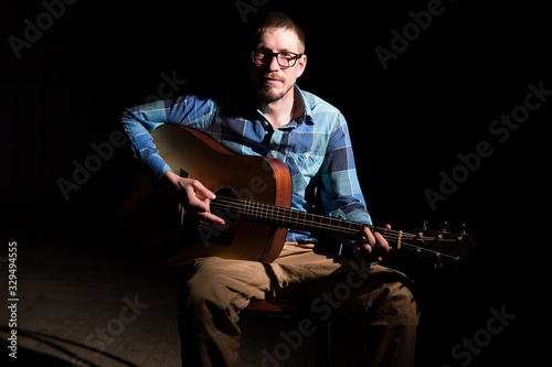 Musician in a plaid shirt plays on an guitar. Low key portrait