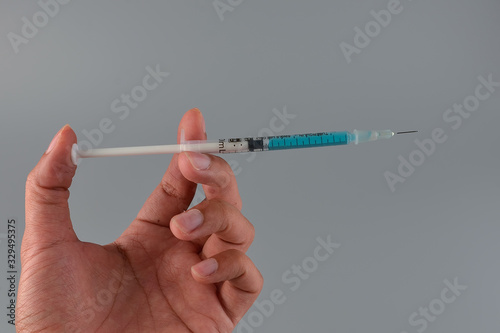 Hand holding vaccine with injection syringe isolated on gray background.