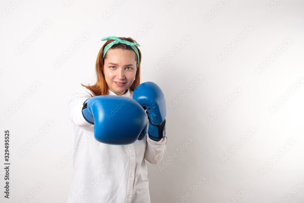 Girl power concept. Confident young woman isolated on a gray wall background. Female and independent power. The girl raises her hand in a boxing glove to strike.Copy space. Girl power concept. Confident young woman isolated on a gray wall background. Female and independent power. The girl raises her hand in a boxing glove to strike.Copy space.