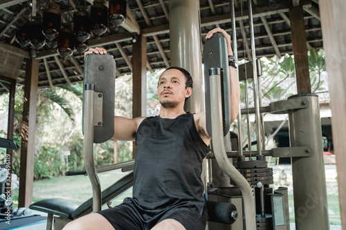 Asian man workout with pec deck machine in the gym house photo