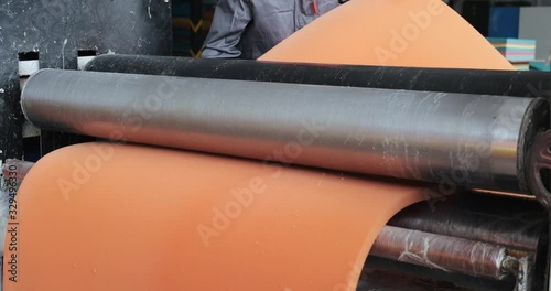 Huge machine with rotating elements in premises of factory floor, two people work with foam blank, rotating wolves compress foam rubber, production of orthopedic mattresses, factory surroundings