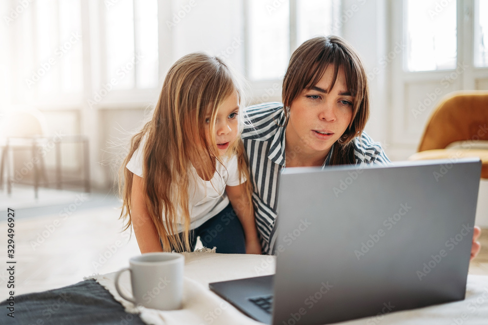 Working mom freelancer with little daughter look to laptop together in bright interior at home Working mom freelancer with little daughter look to laptop together in bright interior at home