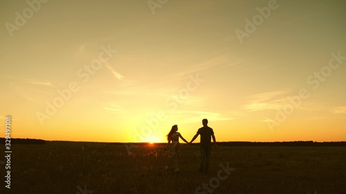 beautiful girl and guy go hand in hand in rays of sun in spring. happy married couple. happy family concept. young couple in love walks and listens to music on a smartphone.