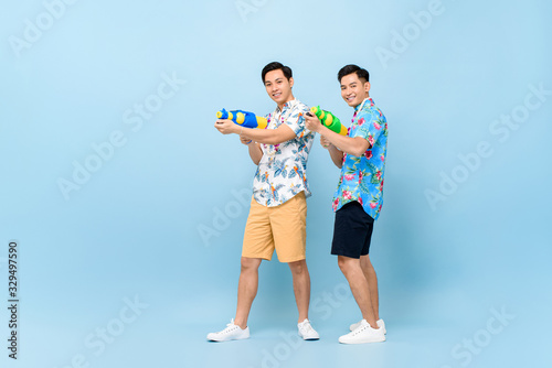 Smilng happy male friends playing with water guns in blue isolated background for Songkran festival in Thailand and southeast Asia