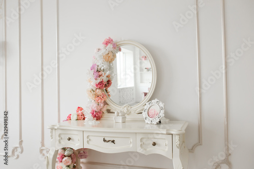 Vintage style boudoir table with round mirror and flowers. White bright room. photo