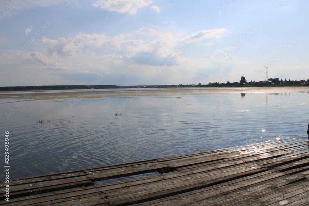 Fototapeta premium Rural pier and lake covered with grass under a blue sky with white clouds