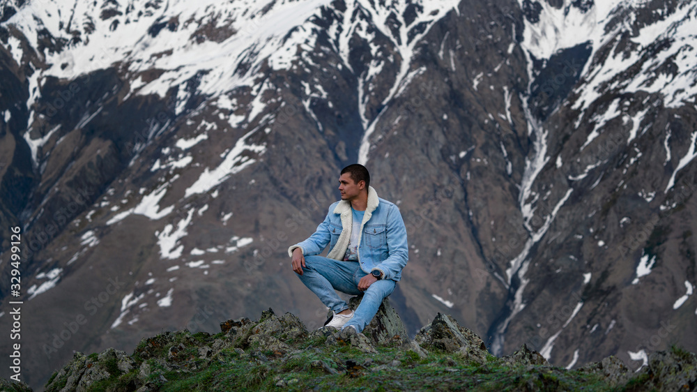 the guy in jeans sitting on a rock mountains in the background