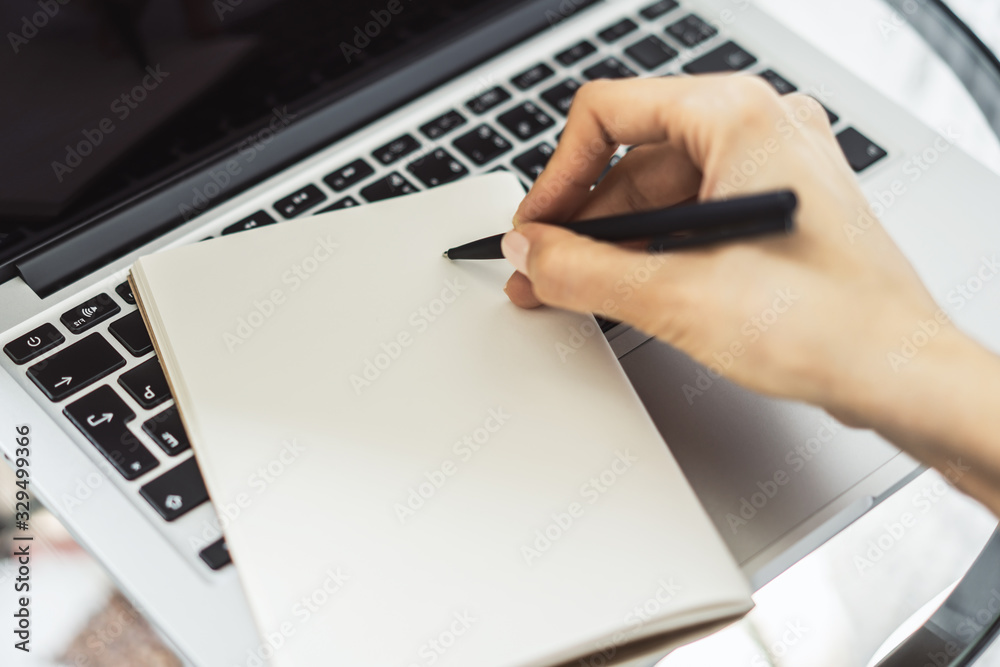 Woman writes with a pen in diary on laptop keyboard in a sunny office, business and education concept. Close up Woman writes with a pen in diary on laptop keyboard in a sunny office, business and education concept. Close up