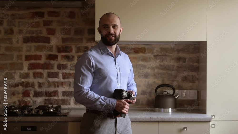 A bald photographer poses with his camera and looks straight with a smile. A man with a beard wears two silver earrings and a blue shirt in the dining room. A bald photographer poses with his camera and looks straight with a smile. A man with a beard wears two silver earrings and a blue shirt in the dining room.