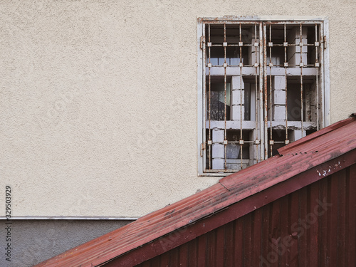 A yellow wall on which an old dirty window with a metal grill is obliquely closed with corrugated rusty iron. Place for an inscription.