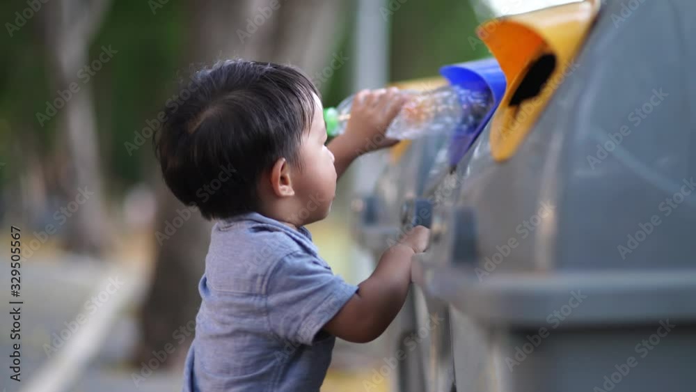 Adorable little boy keep clean plastic water bottle into trash bin in park ecologic world concept