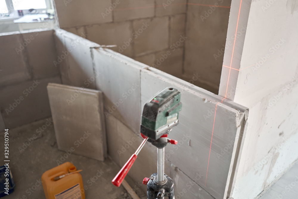 The construction worker Measures horizon level with a laser level. Construction of internal walls in the apartment using a plaster concrete plate with groove ridge. Gypsum plate The construction worker Measures horizon level with a laser level. Construction of internal walls in the apartment using a plaster concrete plate with groove ridge. Gypsum plate