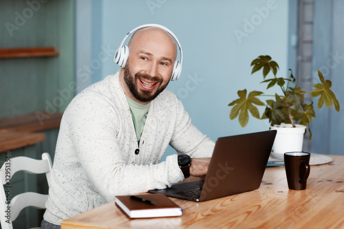 An adult attractive man with headphones is working at the computer in the kitchen. A stylish person enjoys success in business. Work online. Business portrait