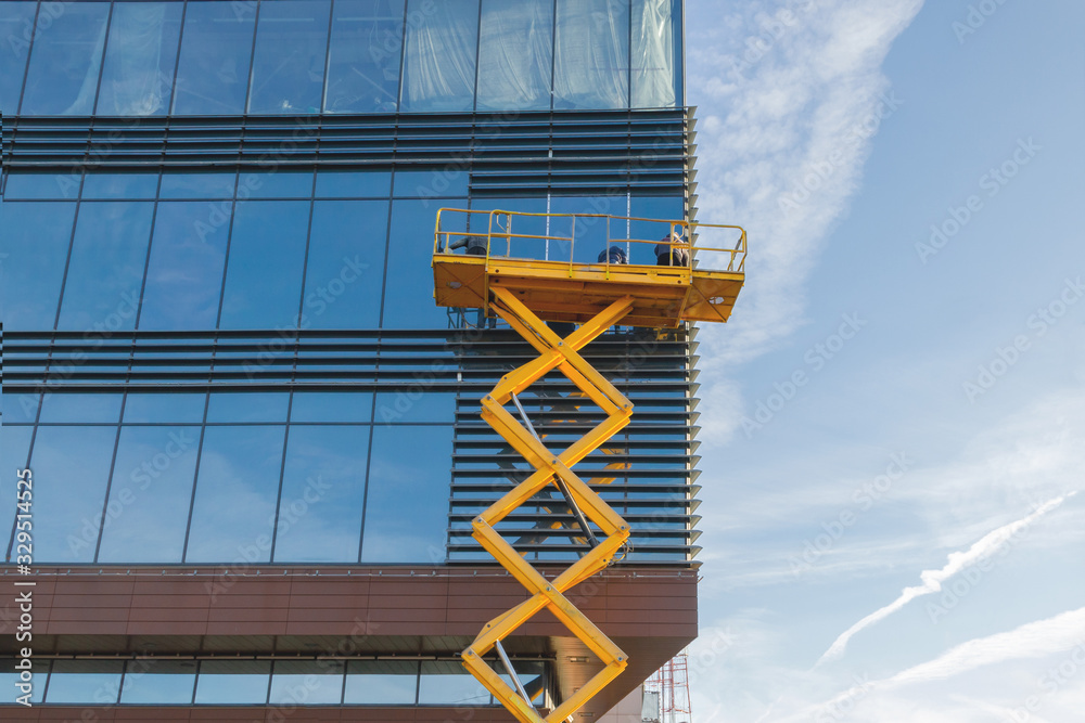 Workers are repairing the glazing in the office building. Scissor lift