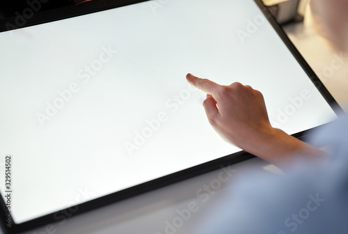 technology and people concept - hand on led light tablet or touch screen at night office photo