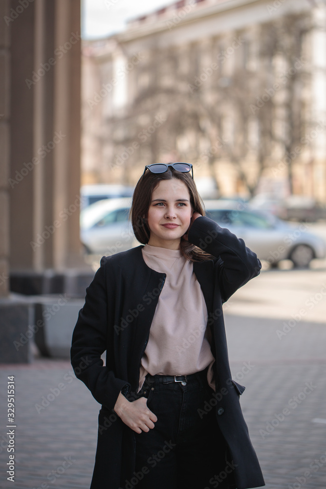 Portrait of a young woman looking at the camera. Beautiful stylish woman in a black coat on a city street. Portrait of a young woman looking at the camera. Beautiful stylish woman in a black coat on a city street.