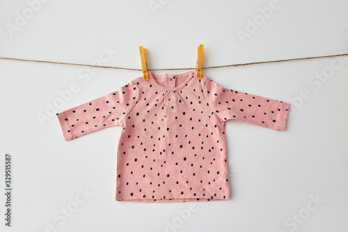 clothes, laundry, babyhood and clothing concept - pink long-sleeved shirt for baby girl with dot print hanging on clothesline with pins on white background