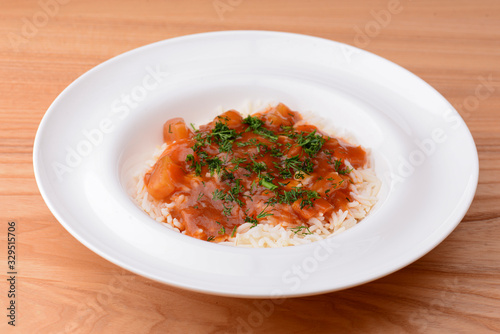 Rice with beef stew with green beans and vegetables served in white plate over light rustic wooden table.
