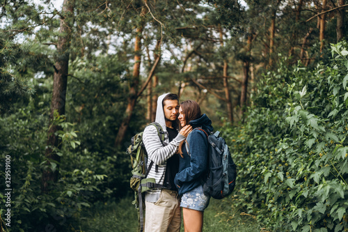 Young couple with backpacks on their backs in the forest. Loving man kisses his beautiful girlfriend on a hike in the woods © bedya