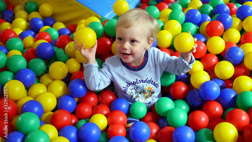 Dziecko wśród kolorowych kulek na placu zabaw w bawialni, chłopiec bawi się kulkami, dziecięce zabawy wśród plastikowych kulek. Trzyma w rękach dwie kulki.