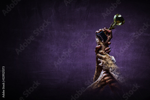 Hand holding up a gold trophy cup against dark background