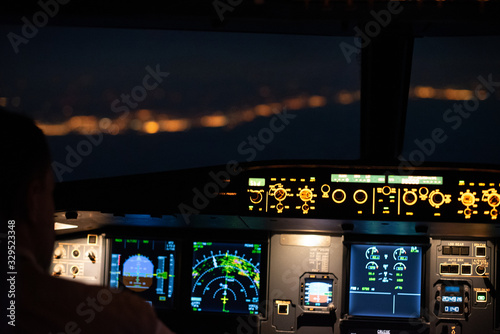 Coastline lit at night seen from the flight deck of a modern airliner, jumpseat view of cockpit with pilot flying