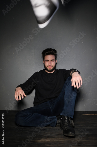 A young dark-haired man with a beard sits on the floor and throws papers and documents into the air. Human emotions: rage, anger, discontent. Close-up studio portrait of a man. © Oleg Samoylov