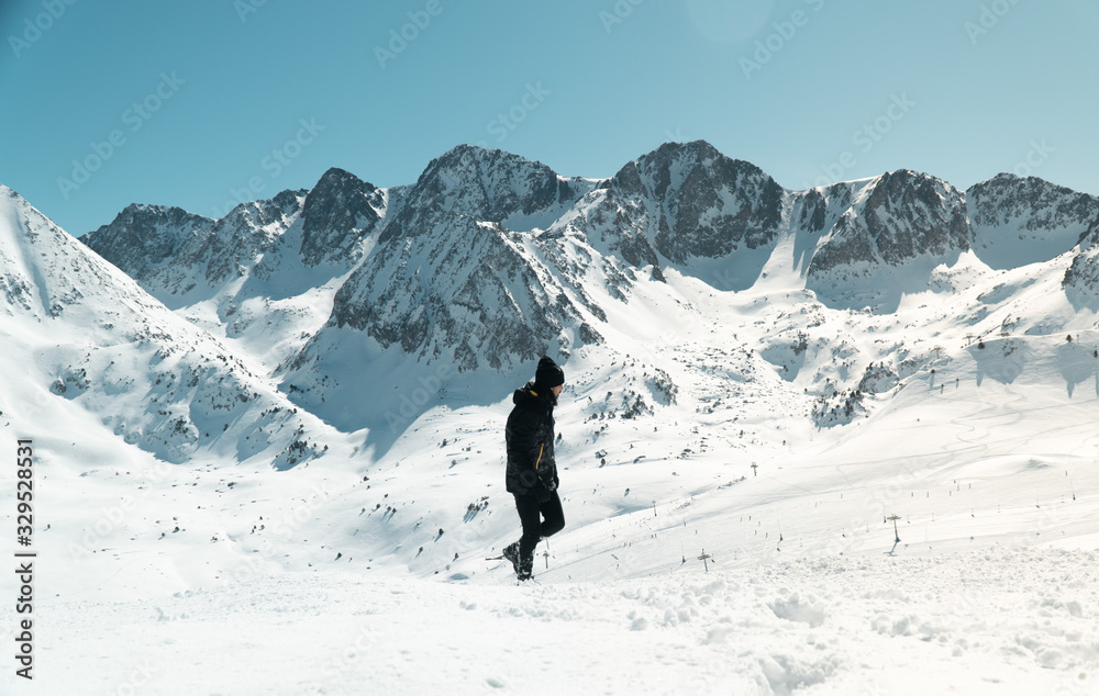 A young man dressed in black walking in the snow on the background of the snow mountain on a sunny day