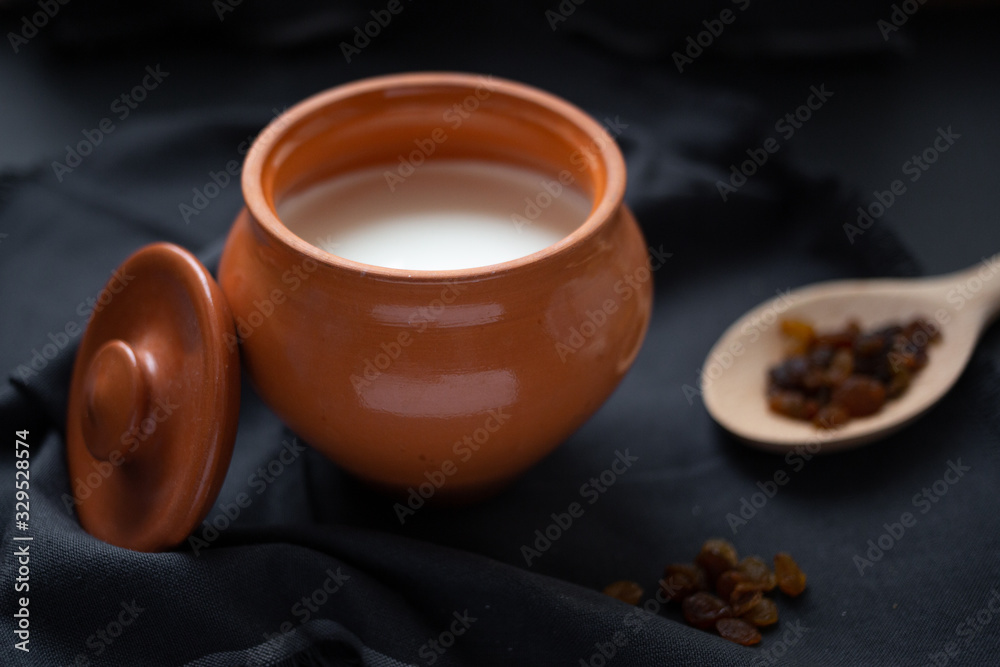Brown pot with sour cream and a wooden spoon with raisins on a dark background. Brown pot with sour cream and a wooden spoon with raisins on a dark background.