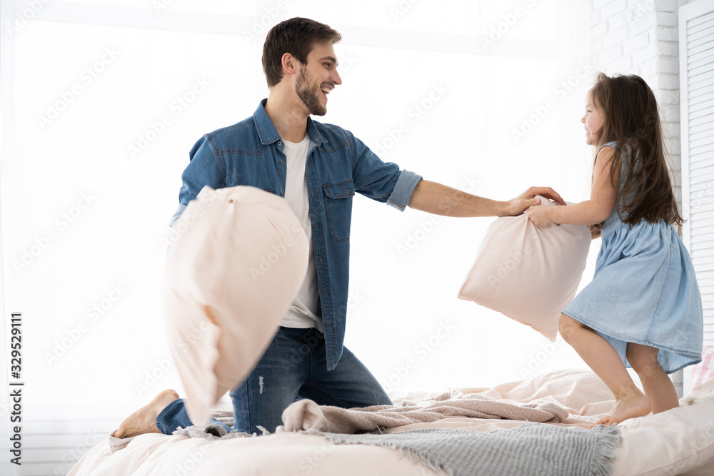 Fototapeta premium happy father and daughter playing pillow fight in bed at morning