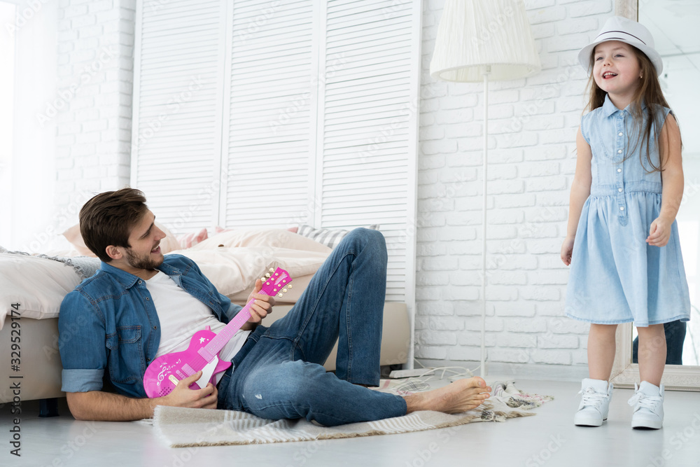 Having fun together. Young father playing guitar for his little daughter and smiling while spending free time at home. Having fun together. Young father playing guitar for his little daughter and smiling while spending free time at home.