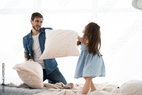 happy father and daughter playing pillow fight in bed at morning