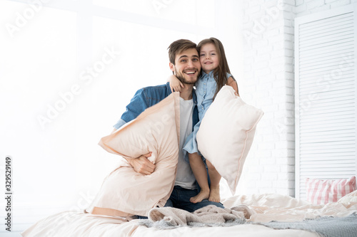 happy father and daughter playing pillow fight in bed at morning