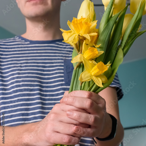 Hands of a man giving a bunch of yellow tulips and daffodils on a turquoise background with copy space