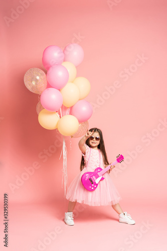 Laughing fashion little girl having fun with guitar isolated on pink background.