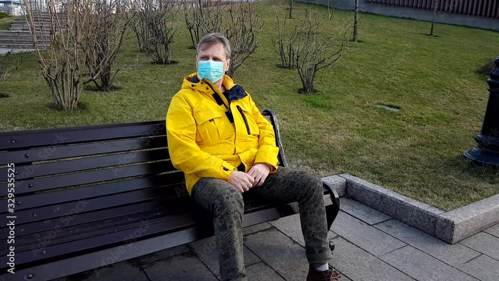 Sick man take on medical mask sitting on a park bench Sick man take on medical mask sitting on a park bench