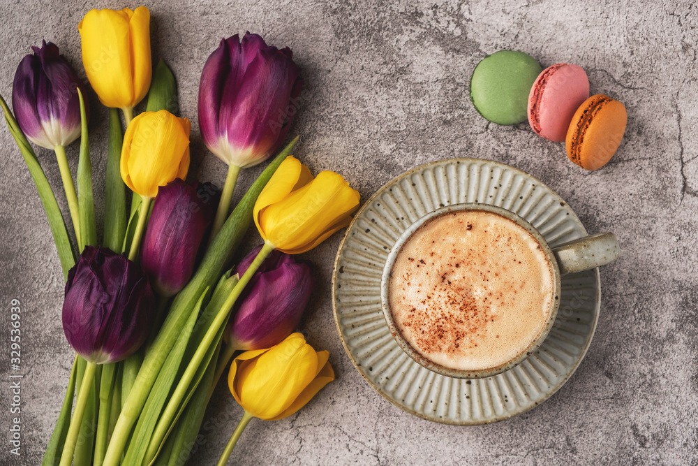 purple and yellow tulips, cup with coffee and macaroon cookies on a gray concrete background, copy space