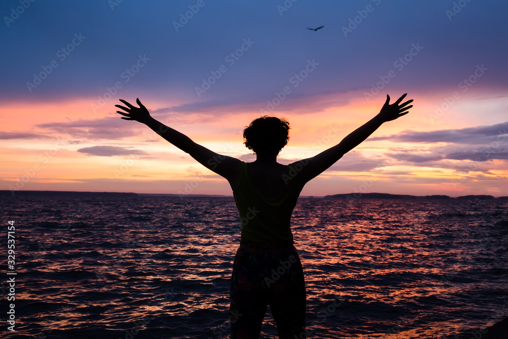 Dark silhouette of a woman on a background of a beautiful sunset sky. Ocean, sunset, man’s power.