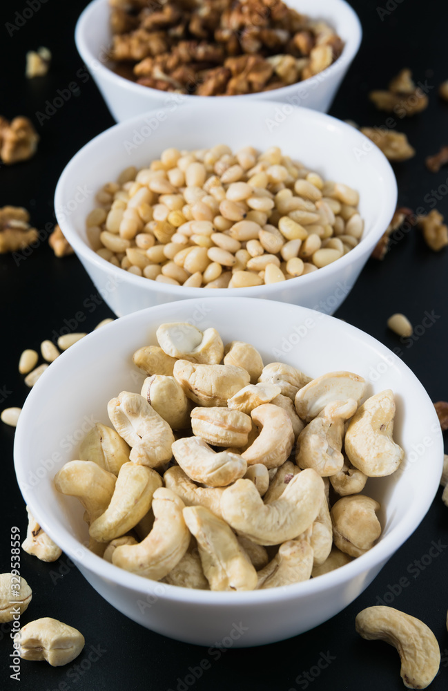 superfood concept, cedar, walnuts, cashew nuts in a plate on a black background superfood concept, cedar, walnuts, cashew nuts in a plate on a black background