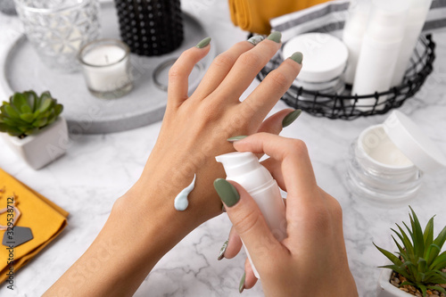 Woman with manicure apply cosmetics on her hand over marble table