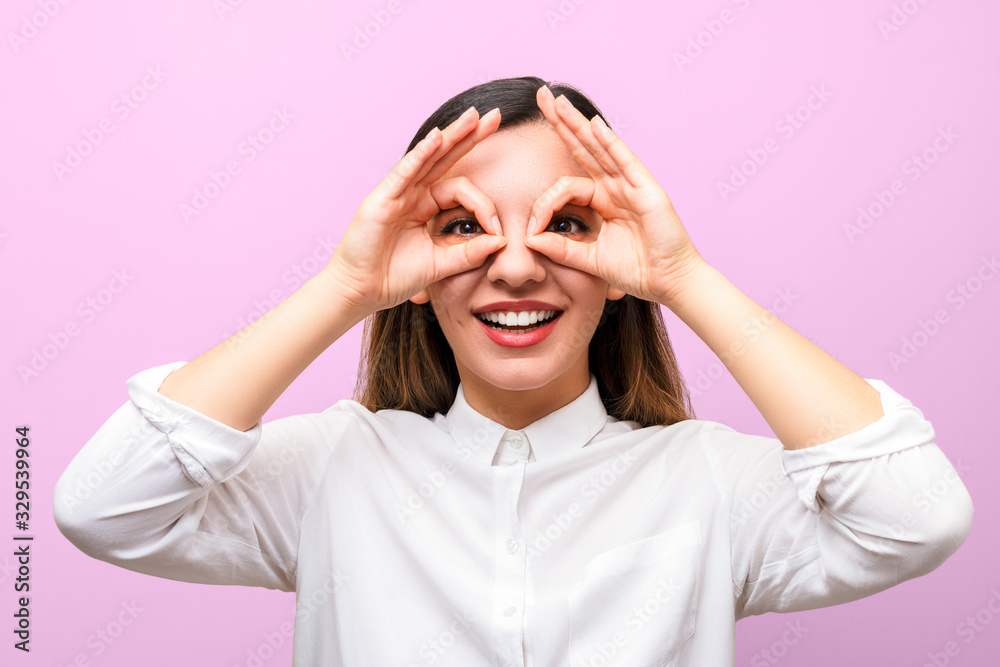 attractive businesswoman or student with red lips in white shirt smiling and making glasses from her fingers against purple background attractive businesswoman or student with red lips in white shirt smiling and making glasses from her fingers against purple background