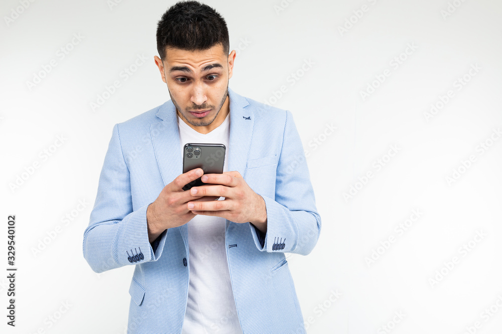 businessman in a blue jacket looks suspiciously at a smartphone on a white background businessman in a blue jacket looks suspiciously at a smartphone on a white background
