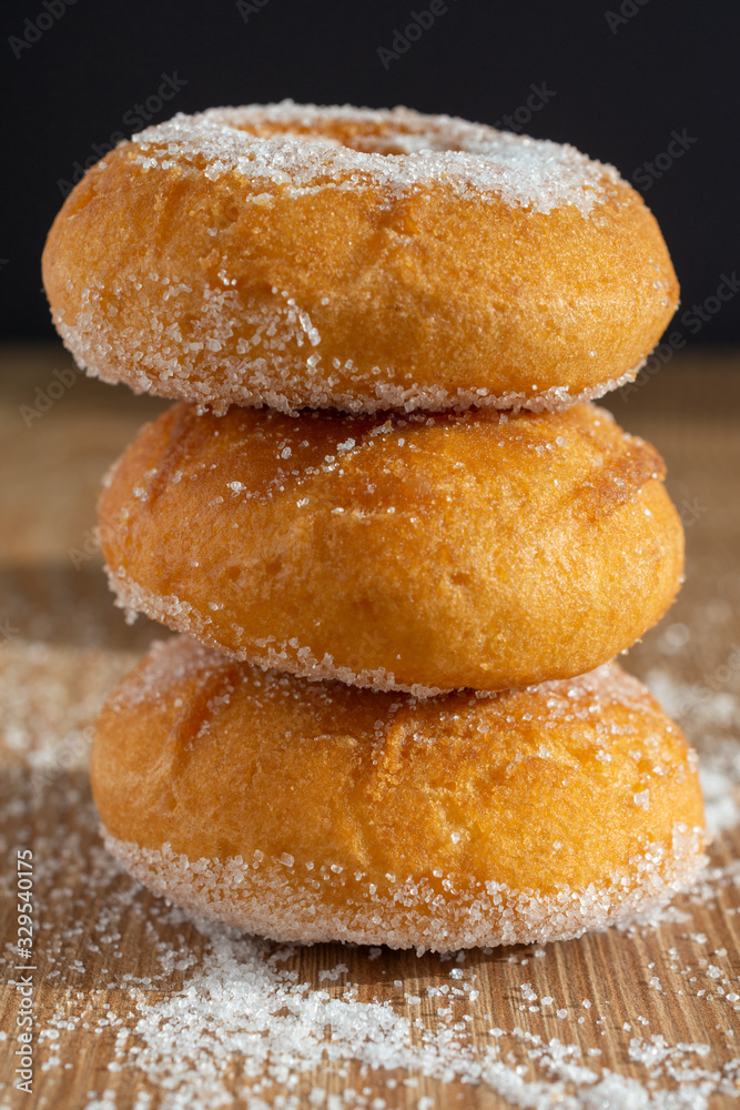 Close-up of three donuts in stack on wooden board with sugar and black background in vertical