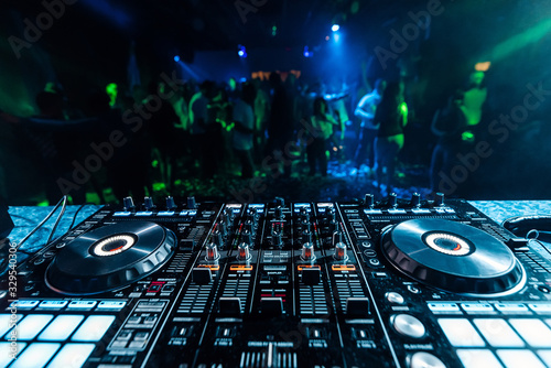 professional music DJ mixer in a booth in a nightclub on the background of blurred silhouettes of dancing people