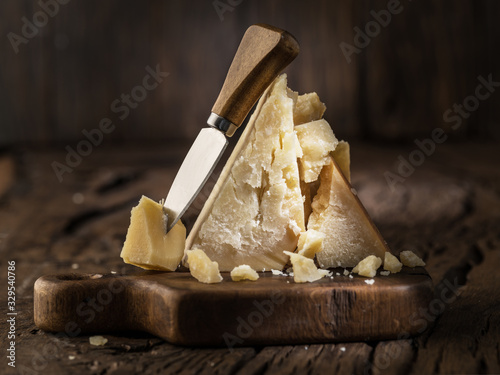 Piece of Parmesan cheese and cheese knife on the wooden board. Dark background.