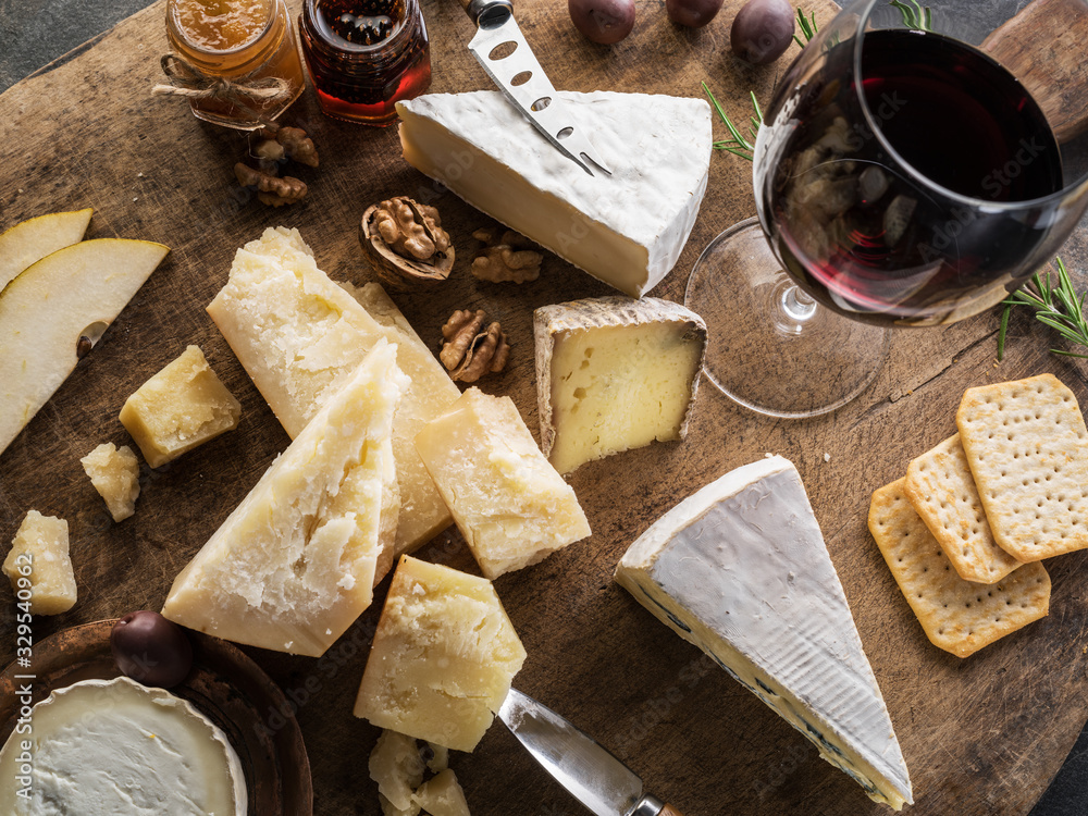 Obraz premium Cheese platter with different cheeses, fruits, nuts and wine on stone background. Top view. Tasty cheese starter.